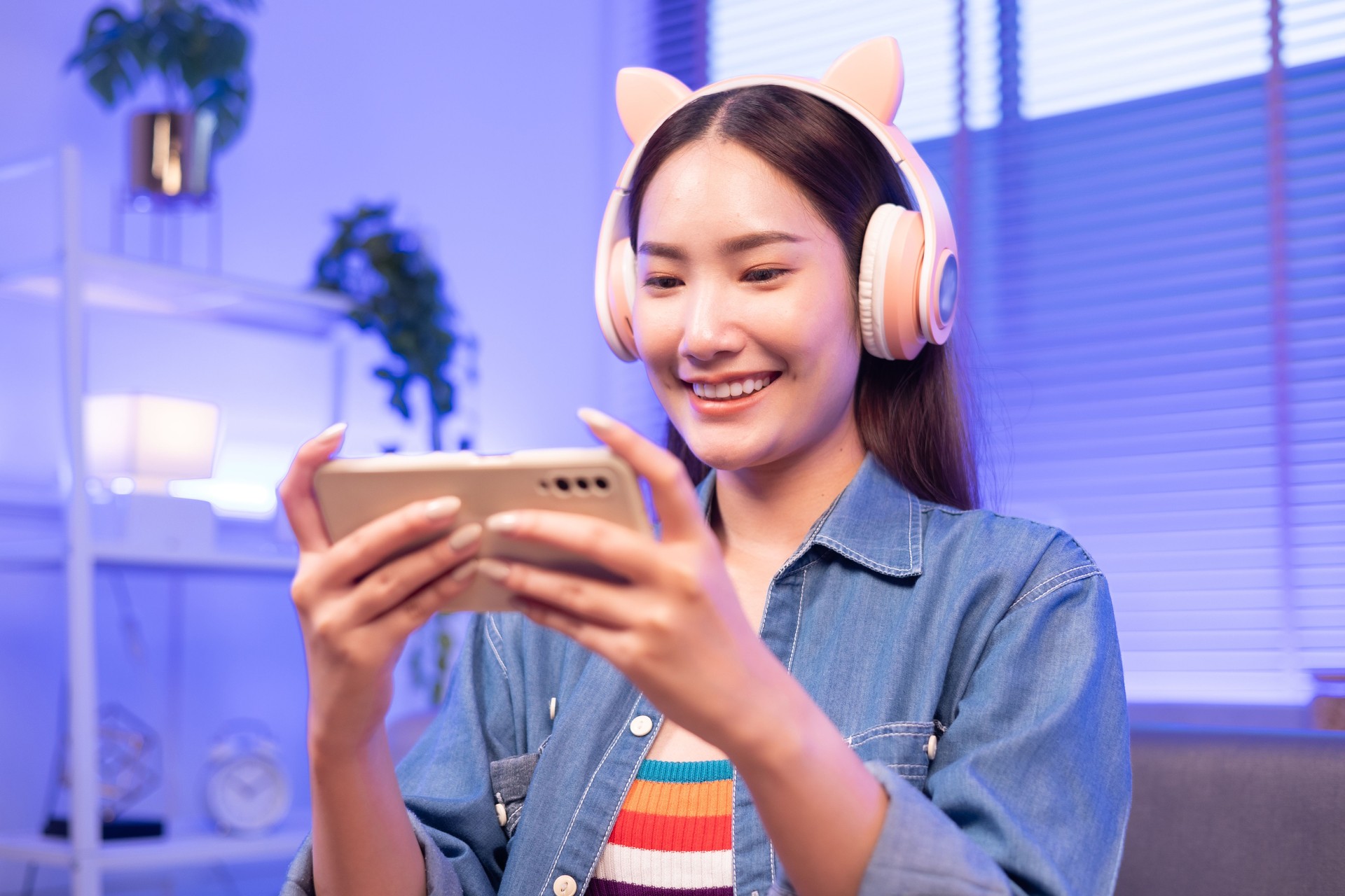 Asian woman gamers revel in their success after emerging victorious in a gaming contest. Seated in armchairs at home, joysticks or mobile in hand, they are bathed in the mesmerizing glow of neon lights in shades of blue and pink.