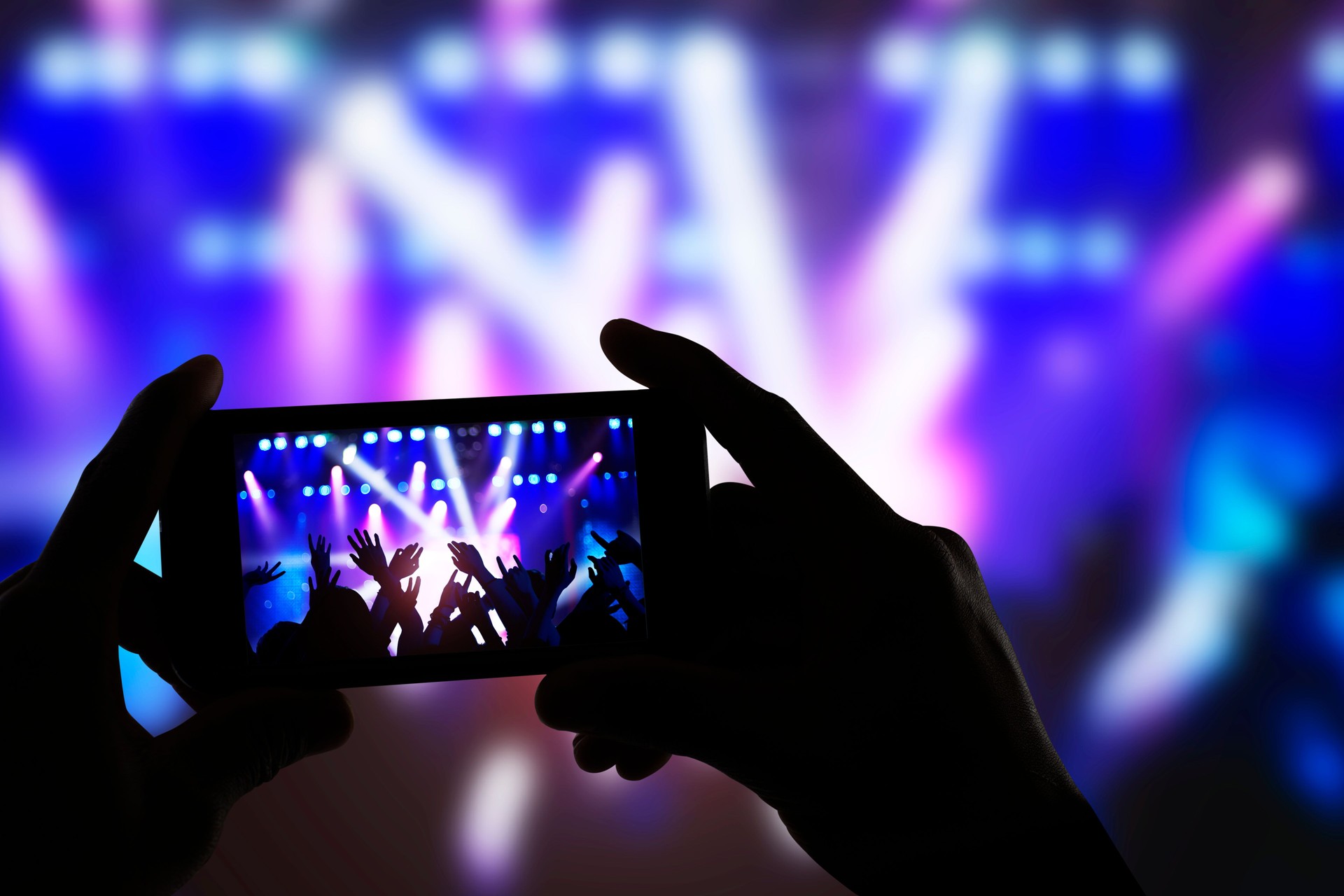Hands holding smart phone and recording concert stage at live music performance